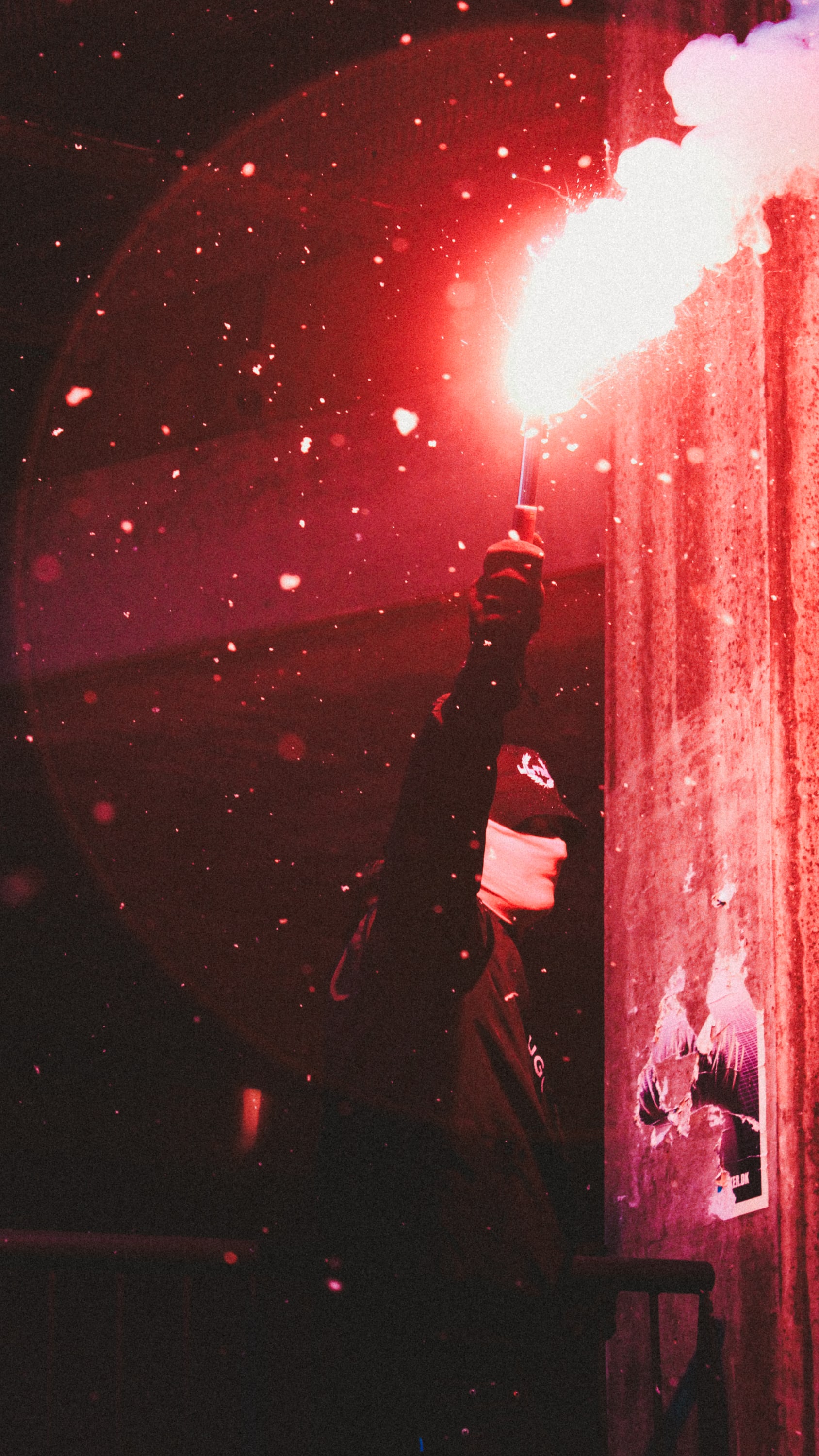 A supporter raises a flare beside a wall as sparks fill the air