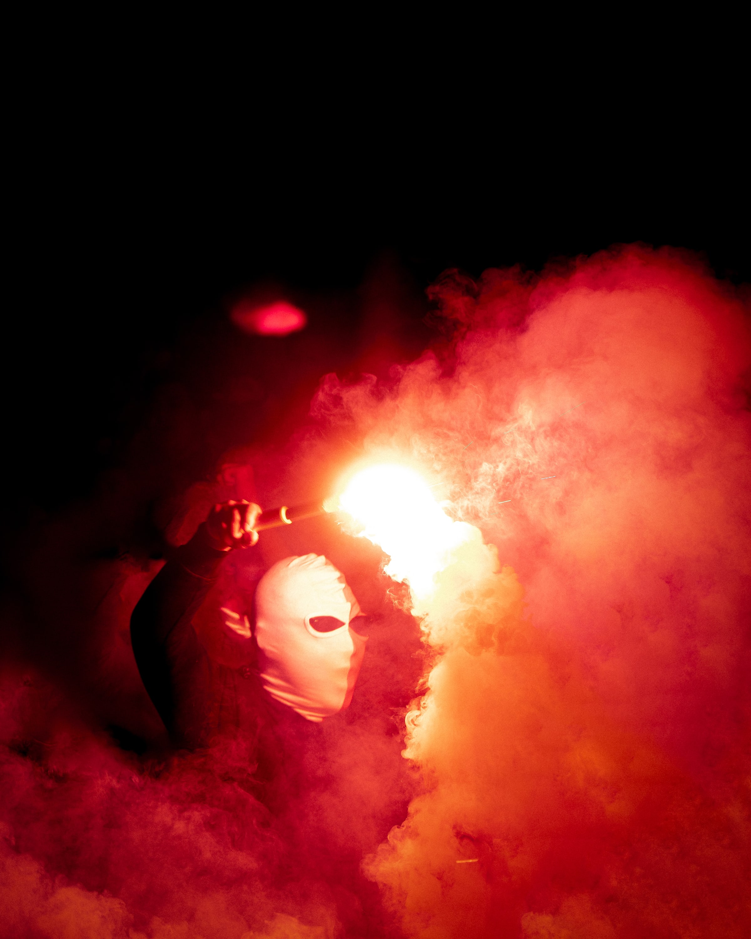 A masked supporter raises a flare into a cloud of orange-red smoke