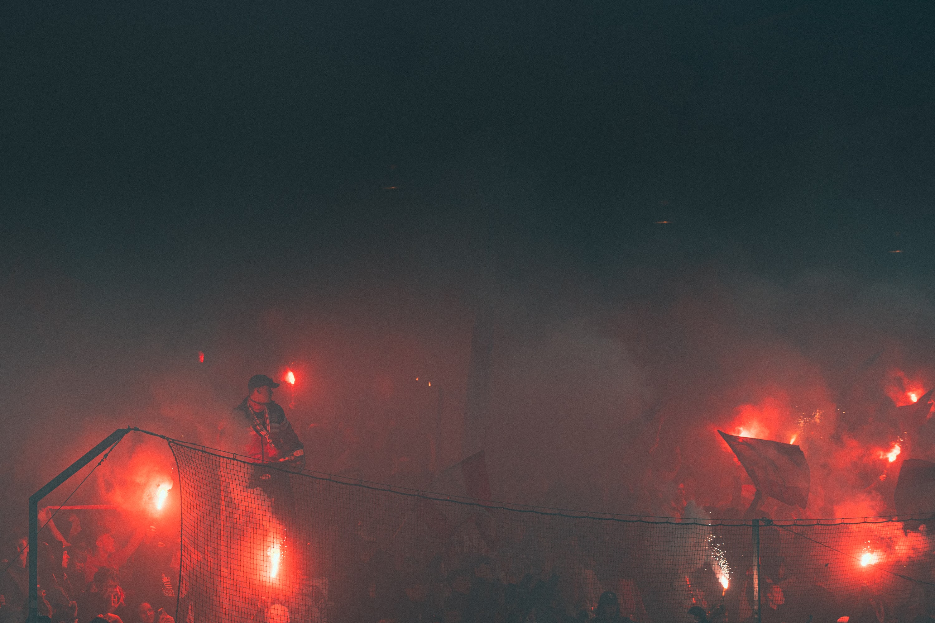 Supporters and flags behind a goal are lit by red flares