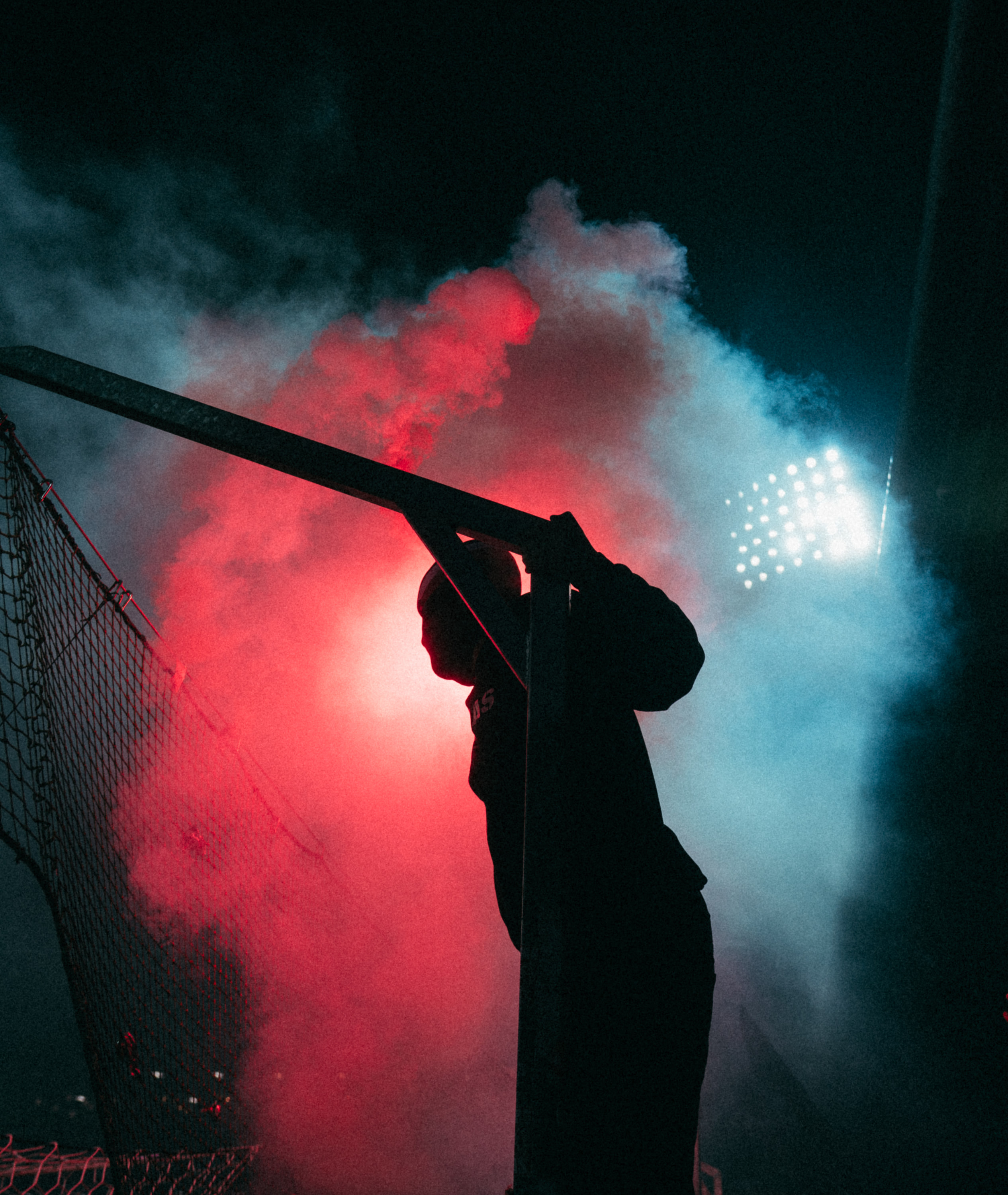 A silhouetted supporter stands amid red and blue flare smoke at night