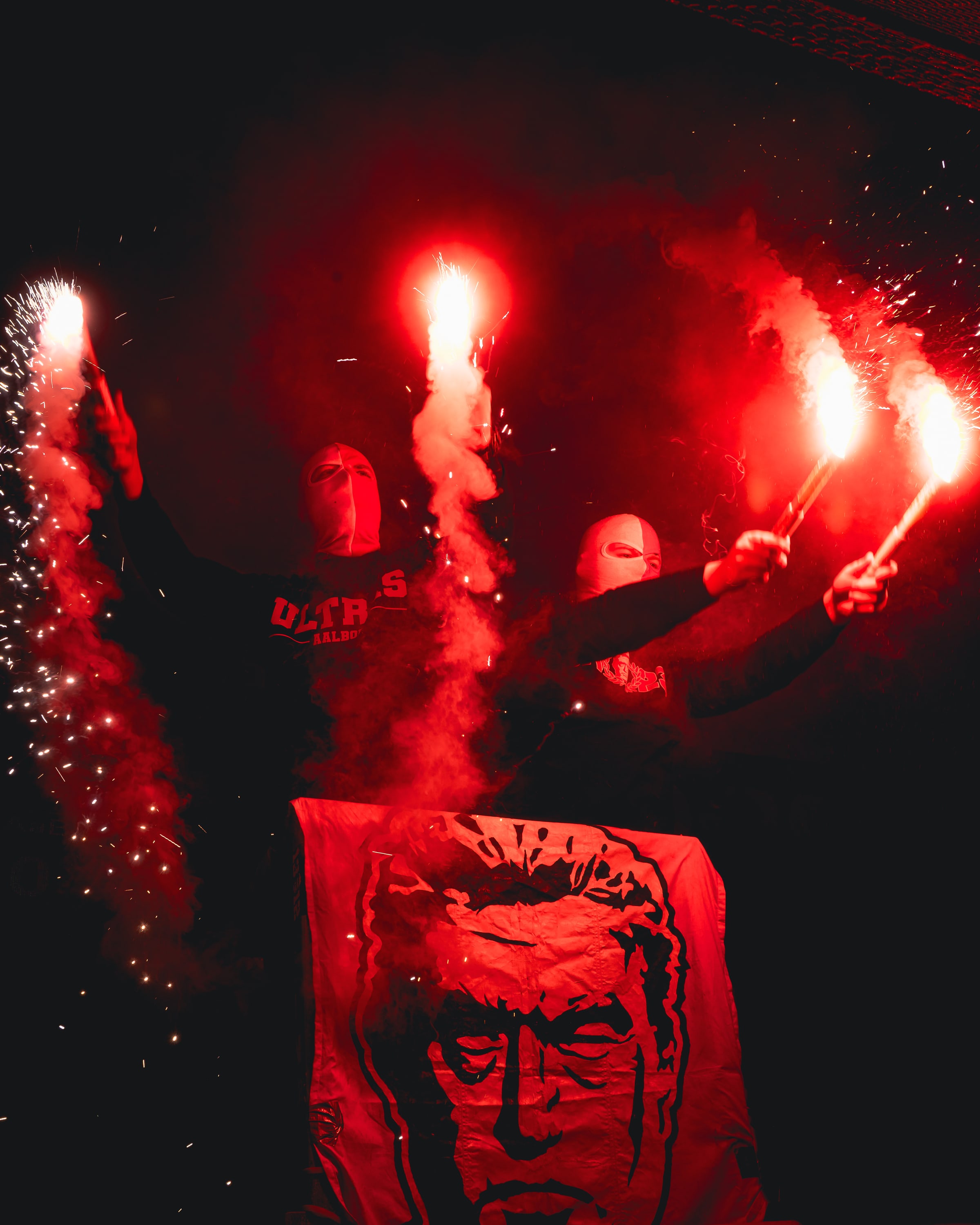 Masked supporters hold burning flares behind a painted banner